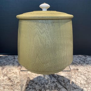 May include: A green wooden storage container with a white knob on the lid. The container is sitting on a clear acrylic stand.