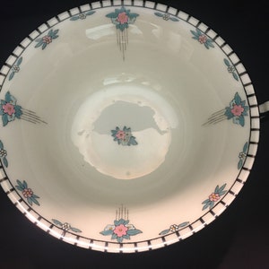 May include: A white porcelain soup bowl with two handles. The bowl has a black and white striped border with a floral design in pink, blue, and green.
