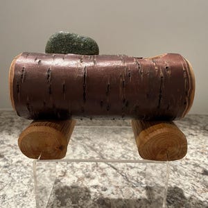 May include: A wooden log with a natural bark texture, resting on two wooden blocks. A green stone sits on top of the log.