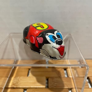 May include: A red, black, and white wind-up toy with a cartoon face and the number "9" on its back. The toy is made of metal and has a key on the bottom to wind it up.