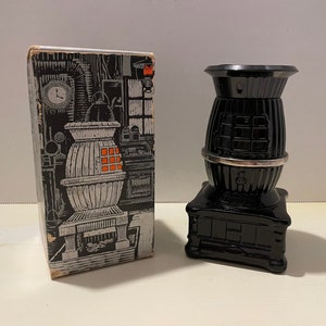 May include: Black glass bottle shaped like a wood-burning stove with a silver band around the middle. The bottle is in its original box with a black and white illustration of a stove on the front.