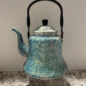 May include: A vintage blue and white speckled enamelware teapot with a black handle and lid. The teapot has a curved spout and a rounded body. The handle is arched and attached to the sides of the pot. The lid has a black knob.