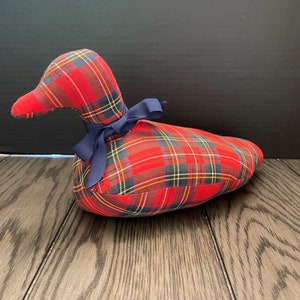 May include: A red and blue plaid duck stuffed animal with a blue ribbon around its neck.