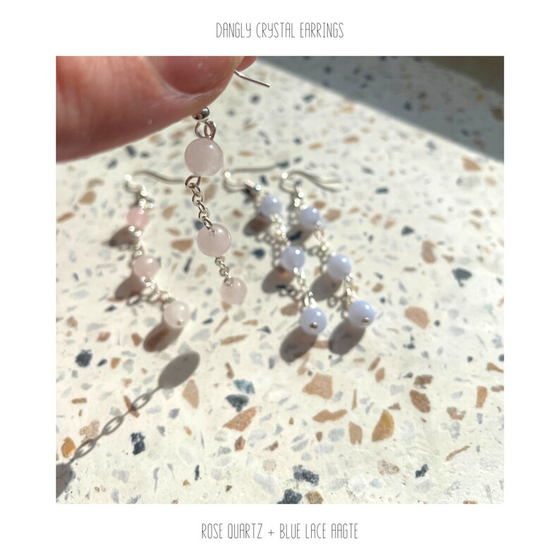 May include: A pair of dangle earrings with silver chains and pink and blue crystal beads. The earrings are labeled "Rose Quartz + Blue Lace Agate".