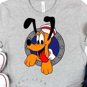 May include: A gray t-shirt with a cartoon image of Pluto wearing a sailor hat and peeking out of a porthole. The text "Aubrey Jean SVG" is printed on the shirt.