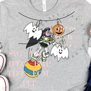 Puede incluir: Una camiseta gris con un diseño de un personaje de dibujos animados, una calabaza y fantasmas. El personaje sostiene una cuerda y está de pie sobre una pelota. El texto "SVG JPEG BMP TIFF  PNG  PDF  PIT" está impreso en la camiseta.