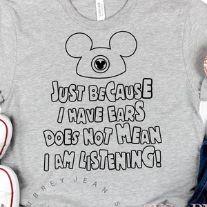 Puede incluir: Camiseta gris con un contorno negro de las orejas de Mickey Mouse y el texto "JUST BECAUSE I HAVE EARS DOES NOT MEAN I AM LISTENING!"