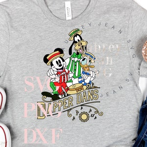 Può includere: Una maglietta grigia con una grafica di Topolino, Paperino e Pippo che suonano musica. Il testo "S'il Vous Plait Dapper Dans Dxf" è stampato sulla maglietta.