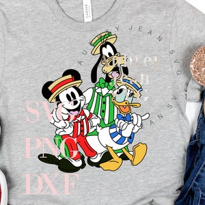 Può includere: Una maglietta grigia con una grafica di Topolino, Paperino e Pippo vestiti con abiti colorati. Il testo "SVG PNG DXF" è stampato in rosa sulla maglietta.