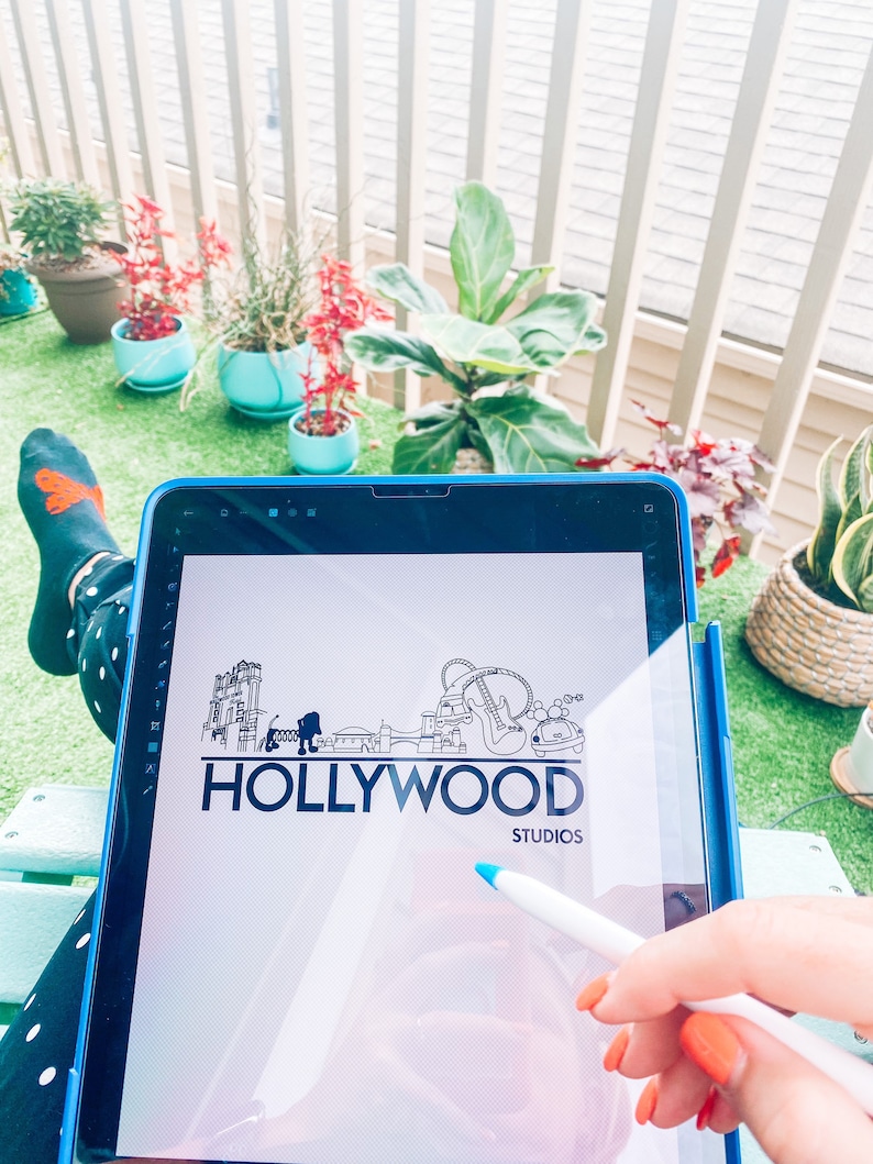 May include: A digital drawing of a Hollywood Studios logo on a tablet screen. The logo is a black and white illustration of a cityscape with the words "HOLLYWOOD STUDIOS" underneath.