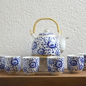 Peut inclure: Tasse en céramique blanche avec une anse noire, portant l'inscription "But First, Coffee" en noir. La tasse est présentée sur un fond flou, suggérant un cadre chaleureux.