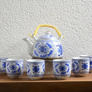 Peut inclure: Service à thé en porcelaine blanche orné de motifs floraux bleus. L'ensemble comprend une théière avec une anse jaune et six tasses assorties. Le design présente des motifs floraux bleus complexes sur fond blanc.