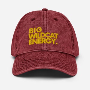 May include: A maroon vintage washed cotton baseball cap with the text "BIG WILDCAT ENERGY." embroidered in yellow.