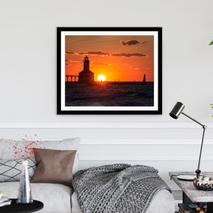 May include: A silhouette of a lighthouse on a pier with the sun setting over the water. The sky is a vibrant orange and pink.