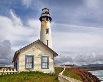 May include: A white lighthouse with a blue trim and a small white house attached to it. The lighthouse is on a cliff overlooking the ocean. The sky is cloudy and the water is choppy.