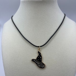 Puede incluir: Collar con un sombrero de bruja negro, ribetes dorados y el texto "Wizard in Training".