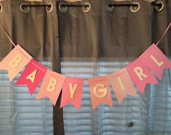 May include: Pink and white banner with gold letters spelling out "BABY GIRL".