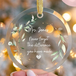 May include: A clear glass ornament with a gold ribbon and a watercolor-style green wreath design. The ornament has the text "Mrs. Jones Never forget The difference you have made" inside the wreath.