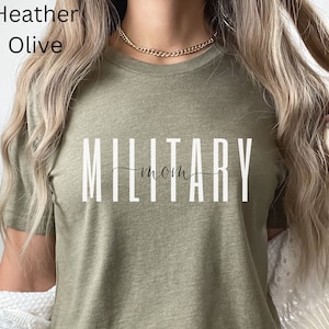 Pode incluir: Uma camiseta verde oliva com o texto "MILITARY mom" impresso em branco.