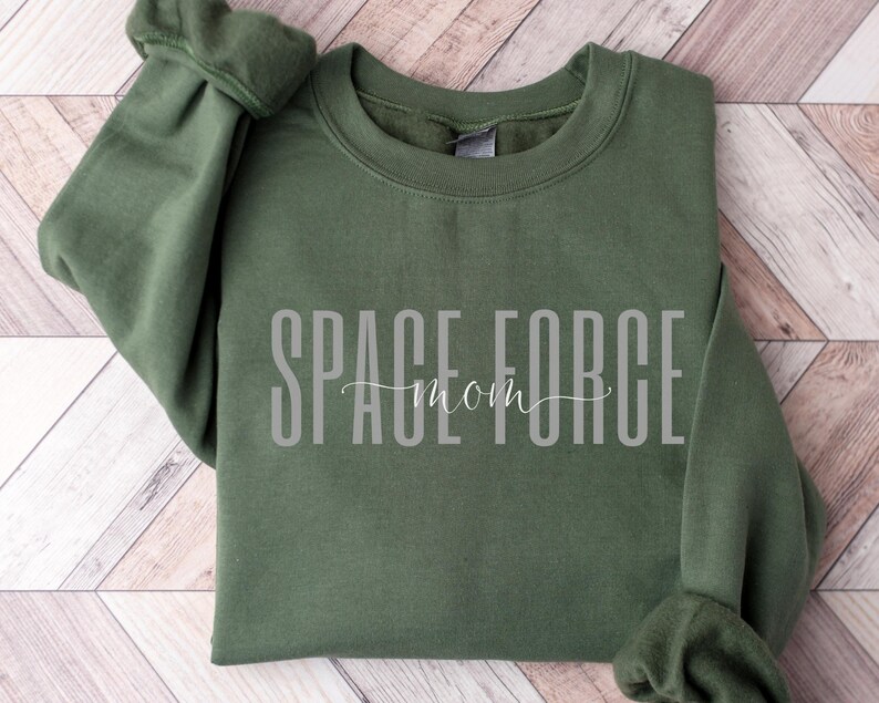 Puede incluir: Una sudadera verde oscuro con el texto "SPACE FORCE mom" en letras blancas.