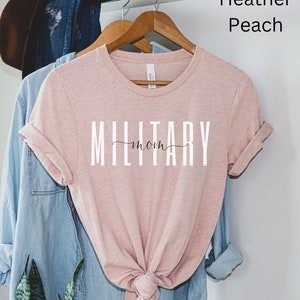 Pode incluir: Uma camiseta cor p&ecirc;ssego com o texto "MILITARY mom" em letras brancas.