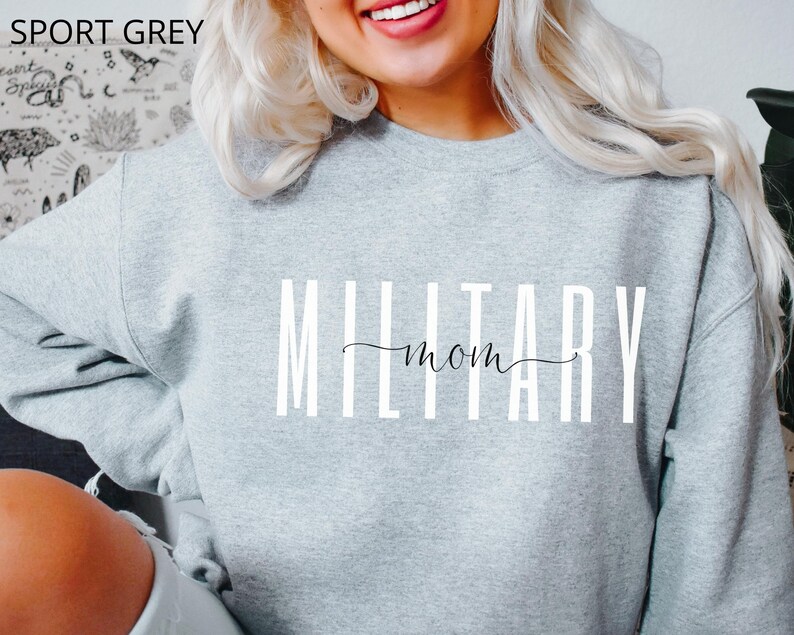 Puede incluir: Una sudadera gris claro con las palabras "MILITARY mom" impresas en blanco. La palabra "mom" est&aacute; en una fuente cursiva. El texto "SPORT GREY" est&aacute; impreso en la esquina superior izquierda de la sudadera.