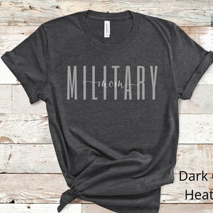 Pode incluir: Camiseta cinza escuro heather com o texto "MILITARY mom" em letras brancas.