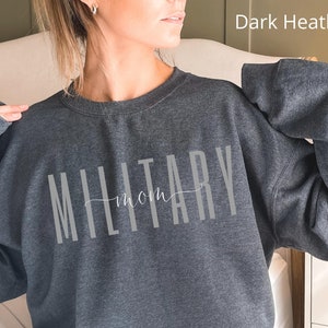 Puede incluir: Sudadera gris oscuro jaspeado con la frase "MILITARY mom" en gris claro. La palabra "MILITARY" est&aacute; en una fuente vertical, con "mom" en un estilo manuscrito. La sudadera es de cuello redondo.