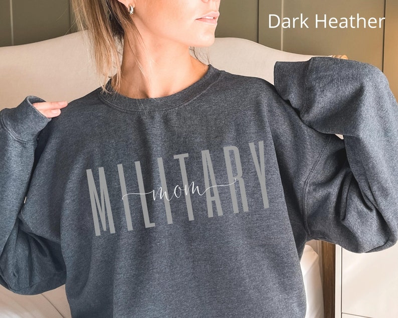Puede incluir: Sudadera gris oscuro jaspeado con la frase "MILITARY mom" en gris claro. La palabra "MILITARY" est&aacute; en una fuente vertical, con "mom" en un estilo manuscrito. La sudadera es de cuello redondo.