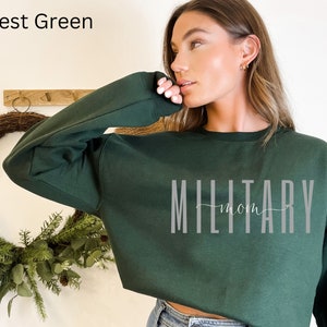 Puede incluir: Sudadera verde bosque con el texto "MILITARY mom" en gris. La sudadera es de color liso y tiene cuello redondo. El texto est&aacute; en una fuente sans-serif con la palabra "mom" en una fuente cursiva.