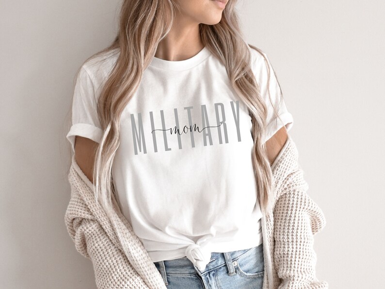 Pode incluir: Camiseta branca com o texto "MILITARY mom" em letras cinzas.