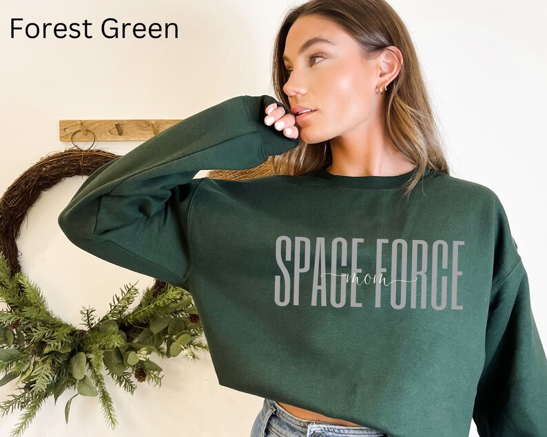 Puede incluir: Sudadera corta de color verde bosque con el texto "SPACE FORCE mom" en blanco.