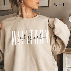 K&ouml;nnte beinhalten: Ein sandfarbener Pullover mit dem Aufdruck "MILITARY girlfriend" in Wei&szlig; auf der Vorderseite.