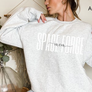 Puede incluir: Sudadera gris ceniza con el texto "Space Force Mom" impreso en blanco.