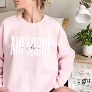 May include: A light pink sweatshirt with the text "AIR FORCE wife" in white letters.