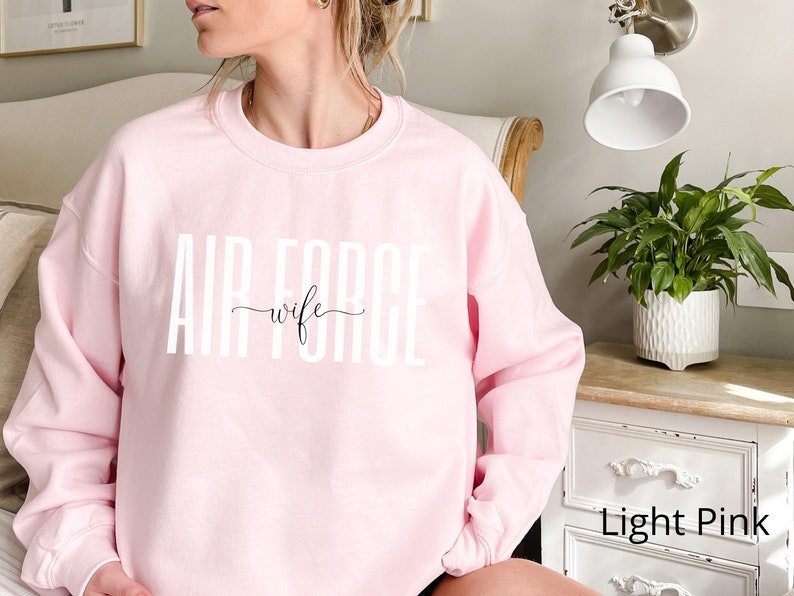May include: A light pink sweatshirt with the text "AIR FORCE wife" in white letters.