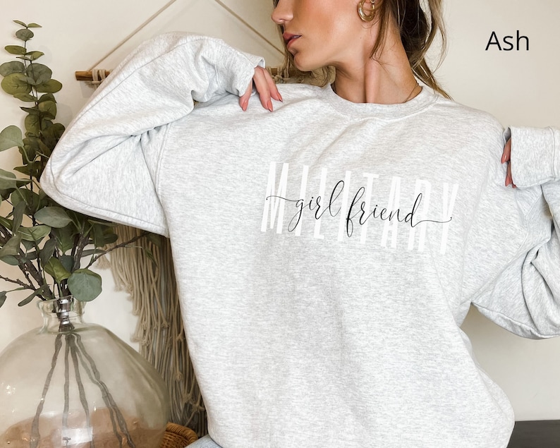 K&ouml;nnte beinhalten: Ein graues Sweatshirt mit dem Aufdruck "Military girlfriend" auf der Vorderseite.