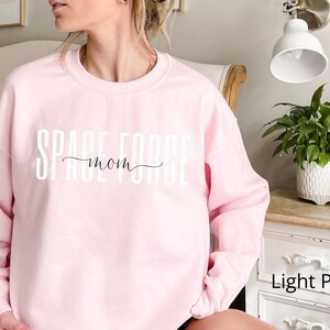 Puede incluir: Sudadera rosa claro con el texto "Space Mom" en letras blancas.