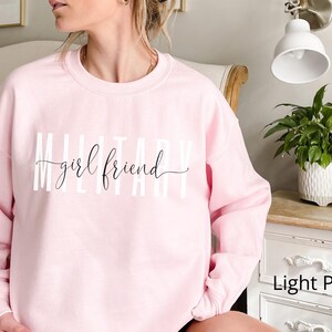 K&ouml;nnte beinhalten: Hellrosafarbener Pullover mit dem Schriftzug "Military girlfriend" in wei&szlig;.