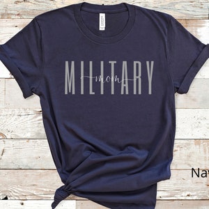 Pode incluir: Camiseta azul marinho com o texto "MILITARY mom" em letras cinzas.