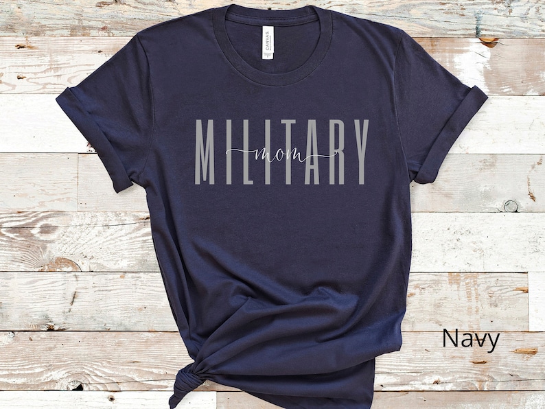 Pode incluir: Camiseta azul marinho com o texto "MILITARY mom" em letras cinzas.