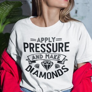 Peut inclure: T-shirt blanc avec un texte noir qui dit "Apply Pressure and Make Diamonds". Le texte est en gras, sans empattement et est entour&eacute; d'une banni&egrave;re d&eacute;corative.