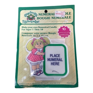 Può includere: Un kit di candele numeriche vintage Cabbage Patch Kids. La confezione presenta un'illustrazione a cartoni animati di un Cabbage Patch Kid che tiene in mano un cartello con la scritta "Place Numeral Here". Il kit include numeri per le età da 1 a 10.