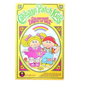 Può includere: Una scatola vintage del set Cabbage Patch Kids Colorforms Dress Up. La scatola presenta illustrazioni di due bambole Cabbage Patch Kids, una ragazza in un vestito rosa e un ragazzo in tuta. La scatola ha uno schema di colori giallo e verde con il testo "Cabbage Patch Kids" e "Colorforms Dress Up Set".