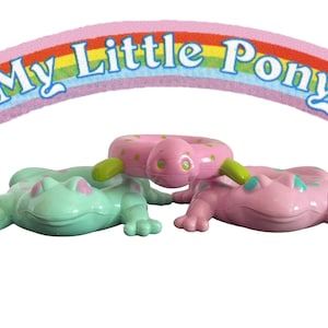 May include: Three My Little Pony frog figurines. One is green with pink spots, one is pink with green spots, and one is a pink and green inflatable ring.
