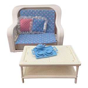 May include: A miniature white wicker sofa with blue floral cushions and two decorative pillows. A matching white wicker coffee table holds a blue tea set on a tray. The set is designed for a dollhouse or miniature display.