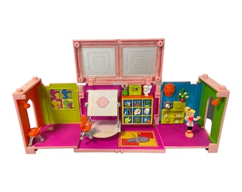 May include: A pink plastic playset with a doll, easel, and art supplies. The playset is open to reveal the interior, which is decorated with colorful walls and a rug. The playset is designed to look like an art studio.