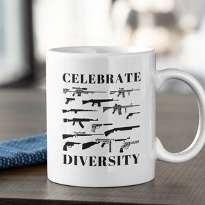 May include: White ceramic coffee mug with a black design. The mug features the text "CELEBRATE DIVERSITY" and a row of various gun silhouettes.