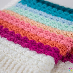 Puede incluir: Una manta de crochet multicolor con rayas blancas, rosas, naranjas, rojas, turquesa y azul claro.