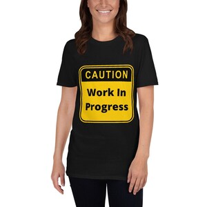 Puede incluir: Camiseta negra con una señal de advertencia amarilla y negra que dice "PRECAUCIÓN Trabajo en curso".